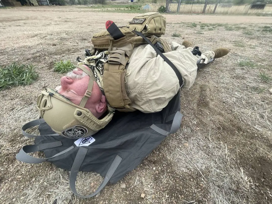 Subject in helmet and pack secured on a deployed Pocket Litter on open ground