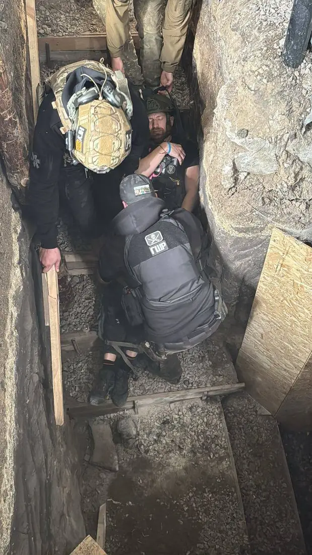 Casualty in a helmet lying on a Pocket Litter at the bottom of a narrow trench